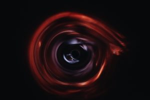 an artist impression of a wormhole reddish rippling space on a black background