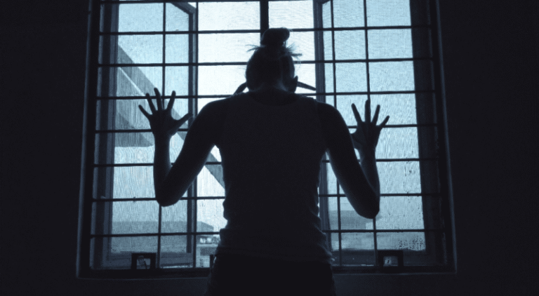 a person with both hands against a barred window