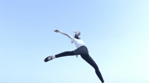 a dancer leaping into the frame against a pure blue sky