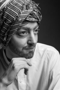 Gillian as a man in a turban looking to the right with hand under chin