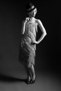 Gillian as a man in a flapper dress and heels in a sassy pose