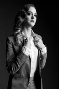 Gillian as a business woman holding her lapels and looking down into the camera