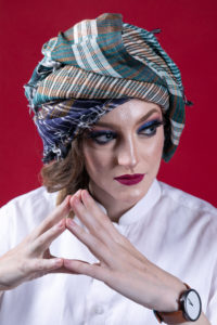 Gillian as a woman wearing a turban and looking to the right with steepled fingers