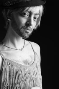 Gillian as a man in a dress looking curiously into the camera