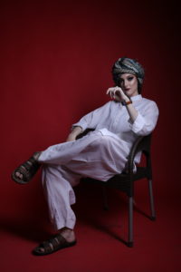 Gillian as a woman in a white salwar kameez with a turban and sitting in a chair