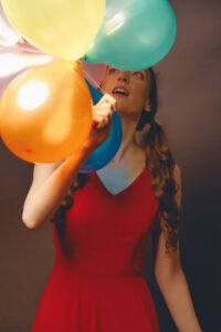 a young girl in red looking up at colorful balloons