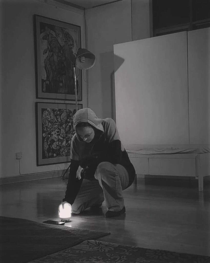 Gillian in a hoodie kneeling with a small lamp