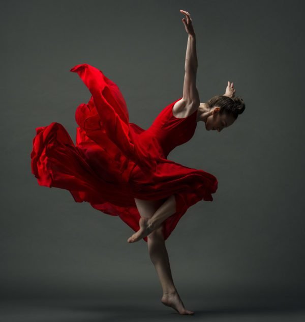 gillian in a red dress and a dynamic posture with head down and arms up behind her, the dress flying up and back