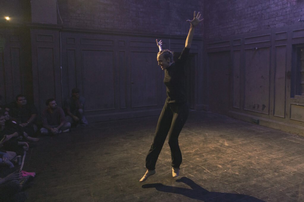 Gillian just about to land a jump facing to the left with arms up and back