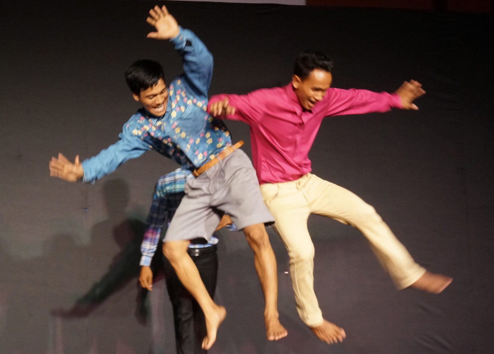 three cambodian dancers jumping and hitting each other in the hip with exuberant expressions