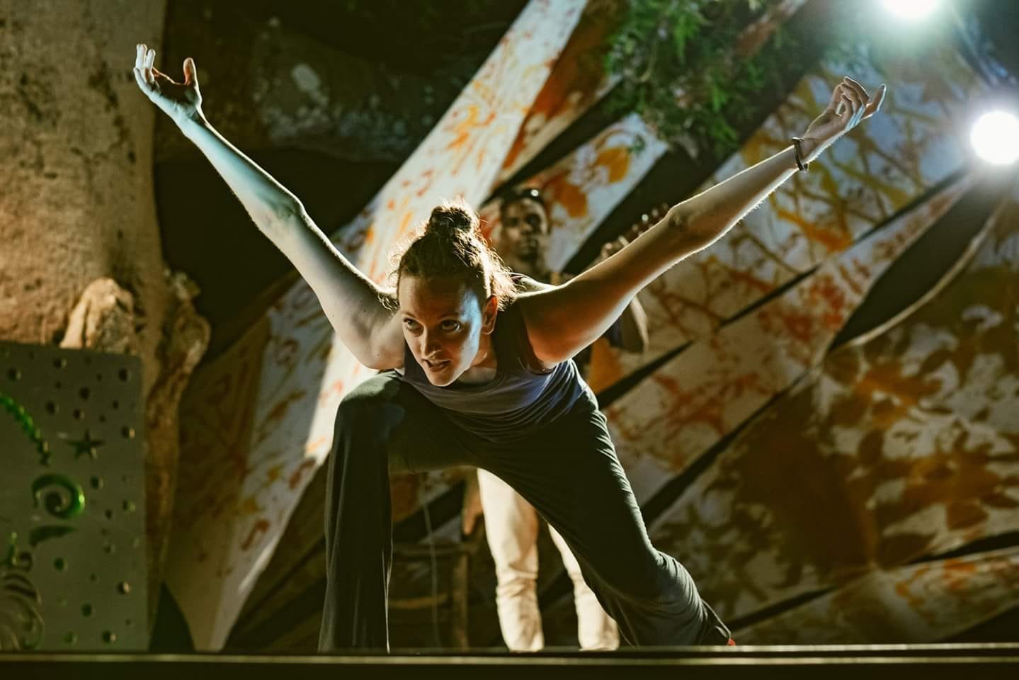 Gillian performing like a dragon against a backdrop of a tree with a guitarist looking on