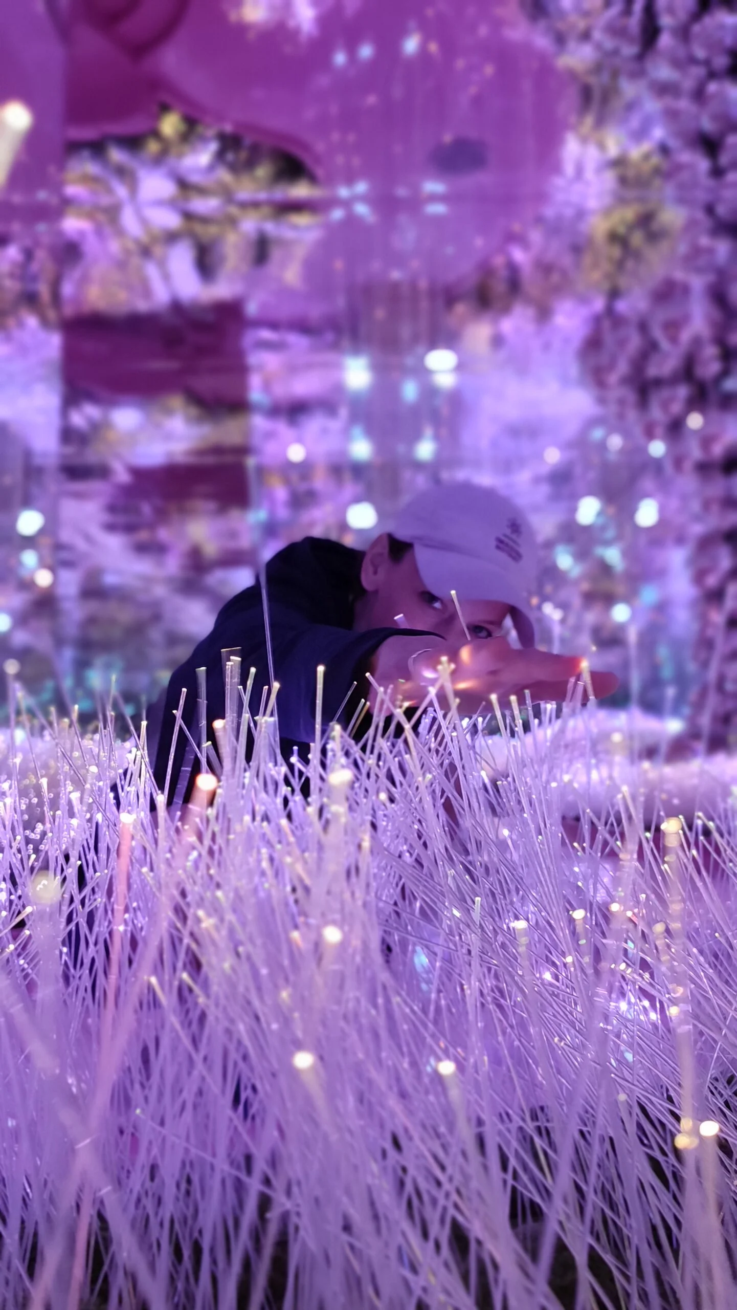 Gillian peering through grass of fiber optic lights with a hand reaching to the camera