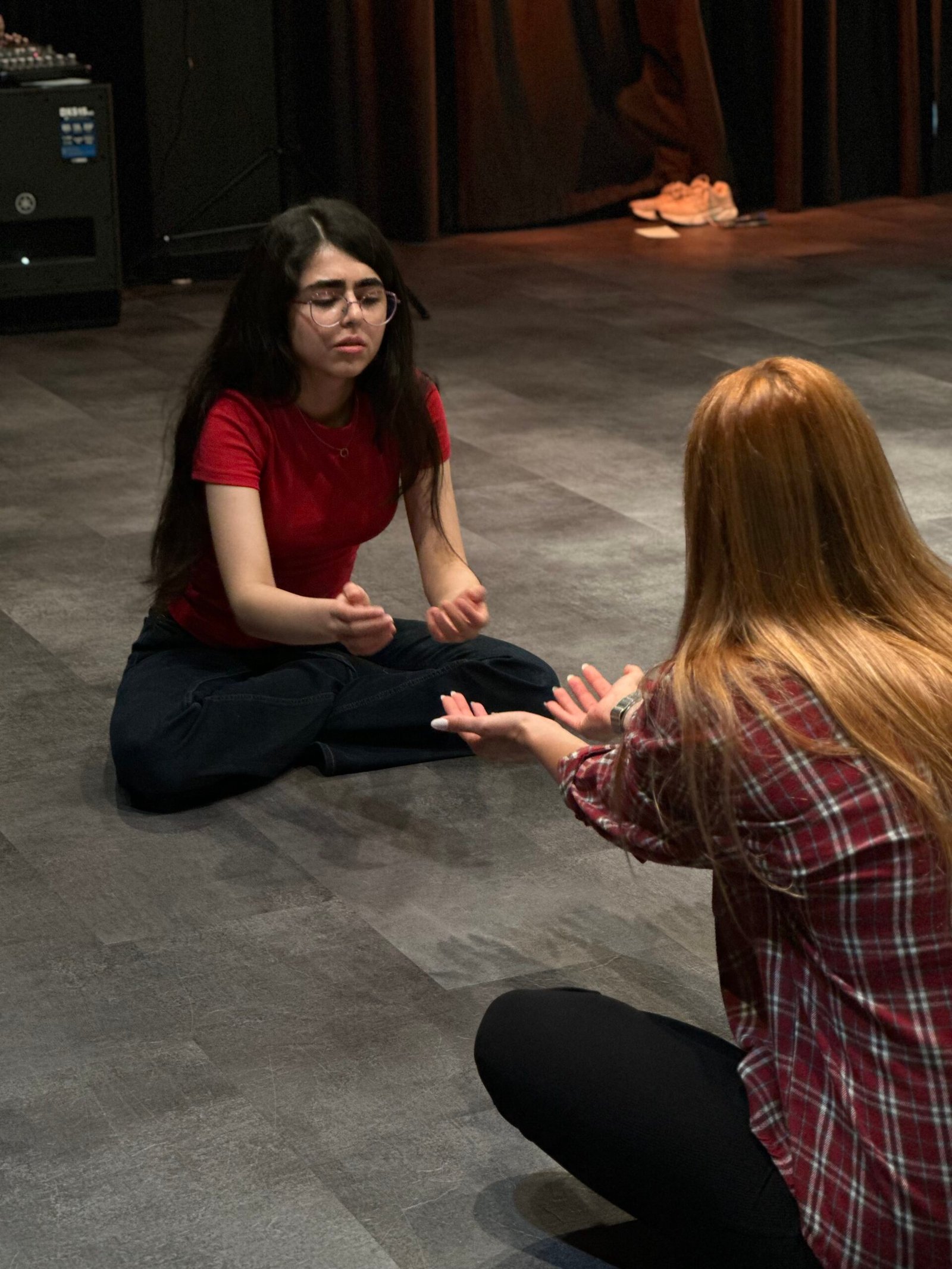 Two women sitting on the floor facing each other and reaching towards the other